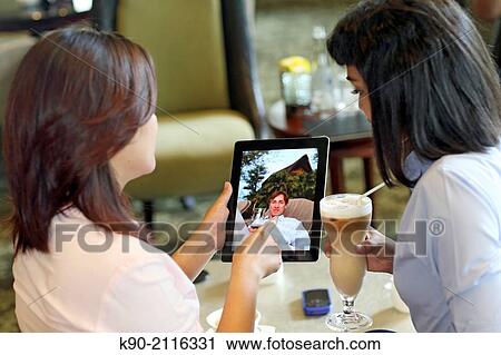 Stock Image - Two asian women holding a tablet computer, Jakarta, Indonesia, Southeast Asia.. Fotosearch