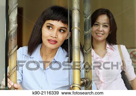 Stock Photo - Two asian women looking out of the entrance door, Jakarta, Indonesia, Southeast Asia.. Fotosearch