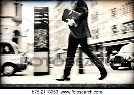 Stock Image - Unrecognizable businessman walking down the street with a folder under his arm. London, England, UK, Europe.. Fotosearch
