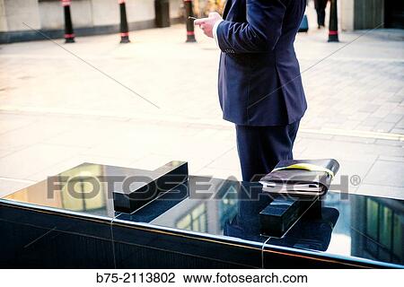 Unrecognizable Executive manipulating a cell phone and his documents folder above a street bench in The City of London, England, UK, Europe. View Large Photo Image Stock Image - Unrecognizable Executive manipulating a cell phone and his documents folder above a street bench in The City of London, England, UK, Europe.. Fotosearch