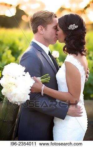 Stock Image - wedding couple embracing and kissing in a vineyard at sunset. Fotosearch