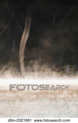 Stock Image - Well defined steam devil moves across a steamy lake in western Iowa on a cool morning. These can be difficult to see, it's easiest when facing more directly at the sun reflection than otherwise.. Fotosearch