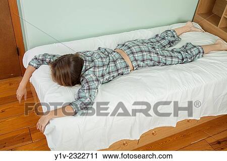 Stock Image - Young woman lying on her bed.. Fotosearch