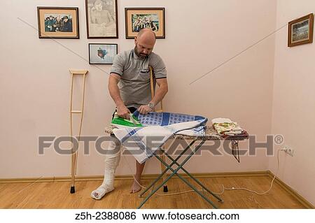 Stock Photograph - A man with a broken leg. Housework.. Fotosearch