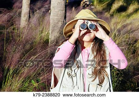 Stock Image - A young girl pretending to be on safari looking through binoculars.. Fotosearch
