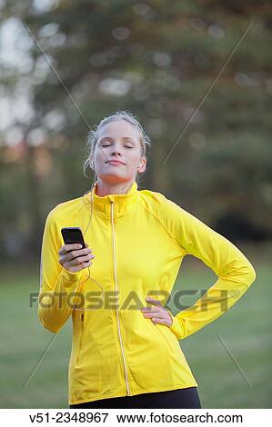 Stock Photo - Blonde woman doing sport in park and listening to music with eyes closed. Fotosearch
