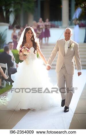 Stock Photo - "bride and groom walking down the ceremony isle, leaving their wedding ceremony, holding hands and smiling". Fotosearch