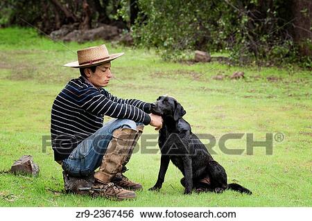 "Chilean cowboy (arriero) pets his black dog as sits on a rock in the valley in El Toyo region of Cajon del Maipo, Chile, South America. " View Large Photo Image Stock Photograph - "Chilean cowboy (arriero) pets his black dog as sits on a rock in the valley in El Toyo region of Cajon del Maipo, Chile, South America. ". Fotosearch