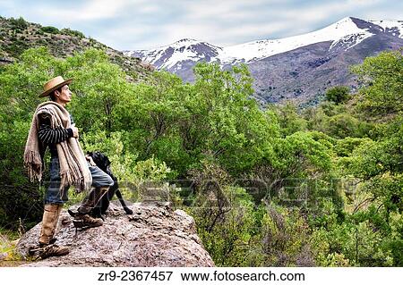 "Chilean cowboy (arriero) stands on a rock and looks out over the Andean mountain with his black dog beside him in the valley in El Toyo region of Cajon del Maipo, Chile, South America. " View Large Photo Image Stock Photo - "Chilean cowboy (arriero) stands on a rock and looks out over the Andean mountain with his black dog beside him in the valley in El Toyo region of Cajon del Maipo, Chile, South America. ". Fotosearch