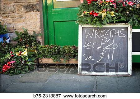 "Christmas wreaths for front door in front of a grocery store with a blackboard that says: wreaths, large 20 pounds, small 11 pounds. Howes, Yorkshire Dales, England, UK, Europe" View Large Photo Image Stock Photo - "Christmas wreaths for front door in front of a grocery store with a blackboard that says: wreaths, large 20 pounds, small 11 pounds. Howes, Yorkshire Dales, England, UK, Europe". Fotosearch