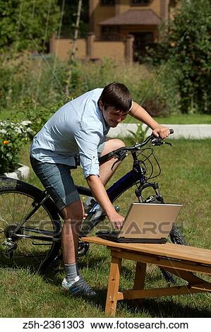 Stock Image - Creative young man with a laptop and a bicycle.. Fotosearch