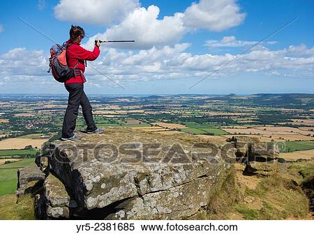Stock Photography - Female walker on The Wainstones at Hasty Bank on The Cleveland Way National Trail looking east with Roseberry Topping and the North Sea in distance. North York Moors National Park, England, United Kingdom.. Fotosearch