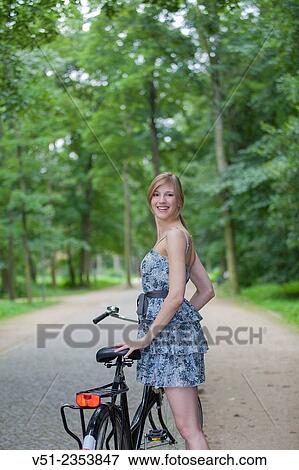 Stock Photo - Happy blonde woman with bicycle in park smiling at camera. Fotosearch