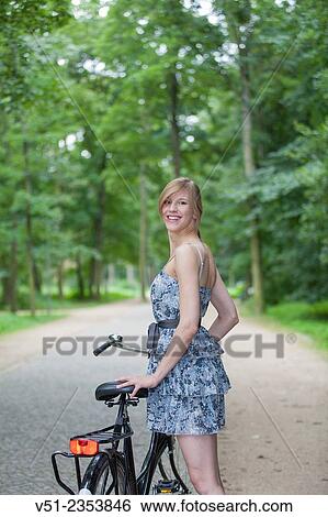 Stock Photograph - Happy blonde woman with bicycle in park smiling at camera. Fotosearch