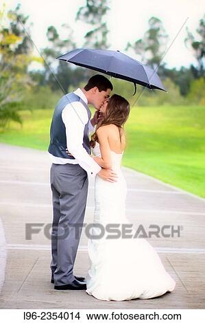 happy couple kissing under an umbrella on a rainy wedding day View Large Photo Image Picture - happy couple kissing under an umbrella on a rainy wedding day. Fotosearch