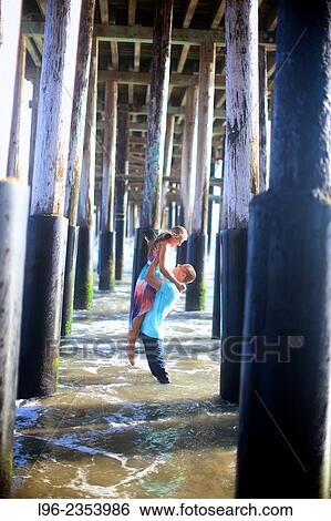 "happy couple where he´s picking her up out of the water, under a pier" View Large Photo Image Stock Photograph - "happy couple where he´s picking her up out of the water, under a pier". Fotosearch