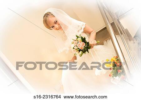 Picture - Happy winking young bride coming down a staircase adorned with roses.. Fotosearch