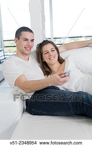 Picture - Happy young couple at sofa enjoying TV. Fotosearch