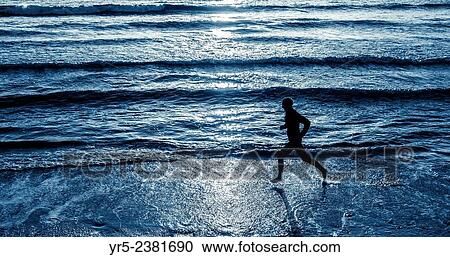 Stock Image - "Man running barefoot along shoreline at sunrise in the North Sea at Seaton Carew, North east England, United Kingdom. ". Fotosearch