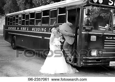 Stock Image - married couple kissing by their wedding bus. Fotosearch
