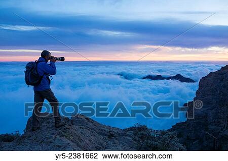 Stock Image - "Photographer at sunset on the highest point on Gran Canaria, Canary Islands, Spain. Pico de Las Nieves 1, 949 metres (6, 394 ft) is the highest point on Gran Canaria. ". Fotosearch