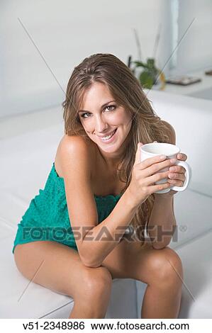 Stock Photograph - Portrait of a blonde woman at home with a cup of coffee smiling at camera in the living room. Fotosearch
