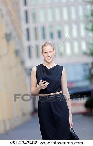 Stock Image - Portrait of a businesswoman in downtown with mobile phone looking at camera. Fotosearch