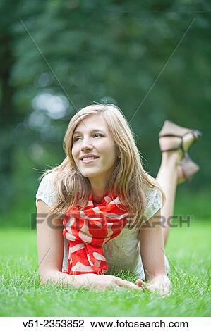 Stock Image - Pretty blonde woman amiling lying down in park. Fotosearch