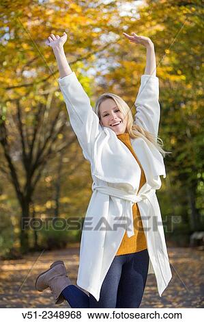 Stock Photo - Pretty blonde young woman walking in Park and smiling at camera with arms raised. Fotosearch