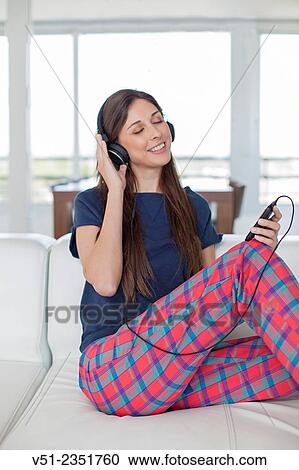 Stock Image - Pretty brunette woman listening to music on the sofa. Fotosearch