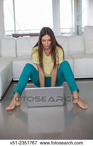 Pretty brunette woman using laptop in the living room View Large Photo Image Stock Photo - Pretty brunette woman using laptop in the living room. Fotosearch