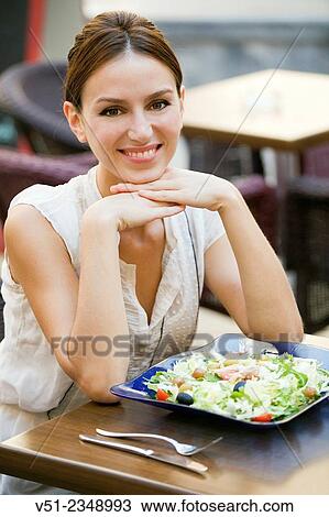 Stock Image - Pretty woman enjoying a salad in a restaurant outdoors smiling at camera. Fotosearch