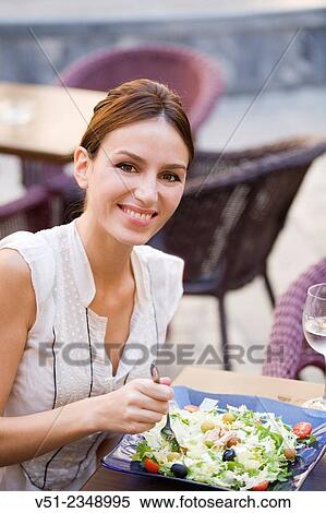 Stock Photography - Pretty woman enjoying a salad in a restaurant outdoors smiling at camera. Fotosearch
