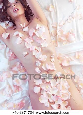 Sensual romantic portrait of a beautiful nude asian woman lying in bed with  pink rose petals covering her naked body. Picture