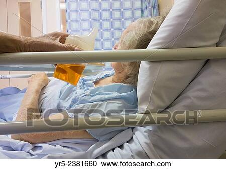 Stock Image - "Son encouraging ninety year old mother to drink fluid in Nation Health Service Hospital in England, United Kingdom. ". Fotosearch