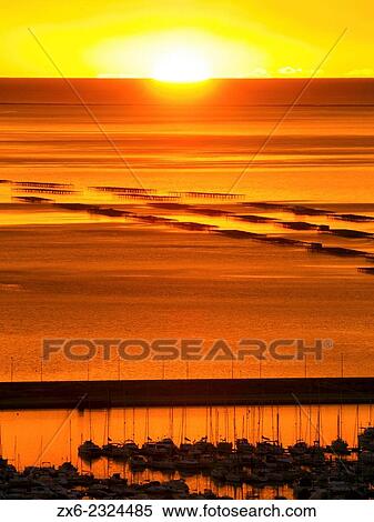 Stock Photography - "Sun appears above the horizon at Mediterranean Sea and Alfacs Bay with mussel breeding platforms. Ebro River Delta Natural Park, Tarragona province, Catalonia, Spain. ". Fotosearch