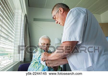 Stock Photography - "Tilburg, Netherlands. Male nurse at an orthopedics nursing ward refreshing the post operative bandages of an elder, female patient. ". Fotosearch