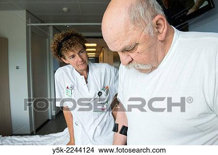 Picture - "Tilburg, Netherlands. Physio therapist instructing a male post operative patient on how to walk again, after reviving a new hip in surgery. ". Fotosearch