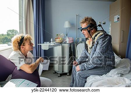 Stock Image - "Tilburg, Netherlands. Physio therapist instructing a post operative patient with fractured cervical on how to walk again, after a head brace is mounted. ". Fotosearch