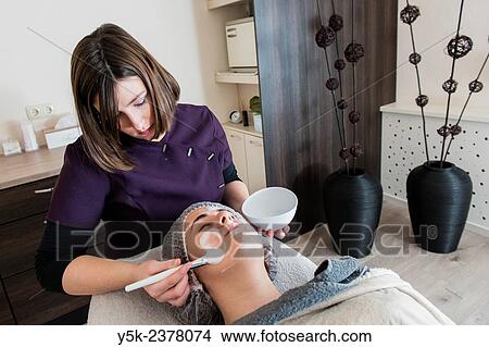 Picture - "Tilburg, Netherlands. Young beautician applying cleansing cream to the facial skin of her customer. ". Fotosearch