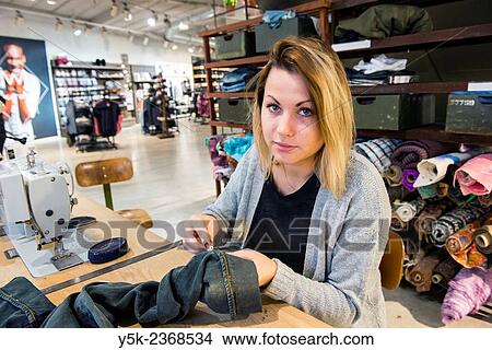 "Tilburg, Netherlands. Young needlewoman buzzy shortening a jeans at her workstation in a fashion store for one of her customers. " View Large Photo Image Picture - "Tilburg, Netherlands. Young needlewoman buzzy shortening a jeans at her workstation in a fashion store for one of her customers. ". Fotosearch
