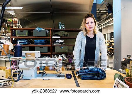 "Tilburg, Netherlands. Young needlewoman preparing to shorten a jeans at her workstation in a fashion store for one of her customers. " View Large Photo Image Stock Photo - "Tilburg, Netherlands. Young needlewoman preparing to shorten a jeans at her workstation in a fashion store for one of her customers. ". Fotosearch