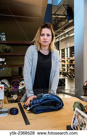 Stock Photo - "Tilburg, Netherlands. Young needlewoman preparing to shorten a jeans at her workstation in a fashion store for one of her customers. ". Fotosearch