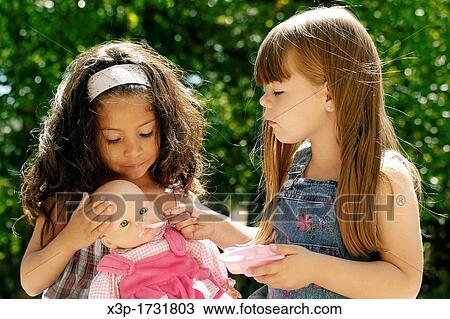 Two little girls feeding a doll View Large Photo Image Stock Image - Two little girls feeding a doll. Fotosearch