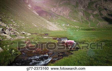 Stock Image - "Woman drinking at a mountain creek, Canton of Graubünden, Switzerland". Fotosearch