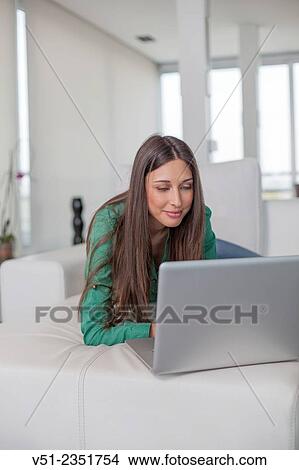 Picture - Woman using laptop on sofa. Fotosearch