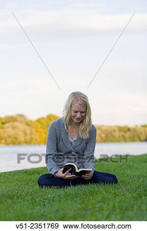 Young blonde woman reading a book by the river View Large Photo Image Stock Photo - Young blonde woman reading a book by the river. Fotosearch