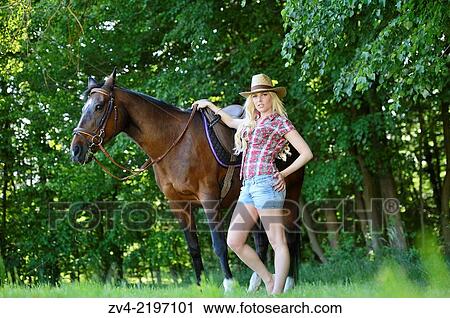 Stock Image - Young cowgirl with a polish arabian horse standing on a meadow.. Fotosearch