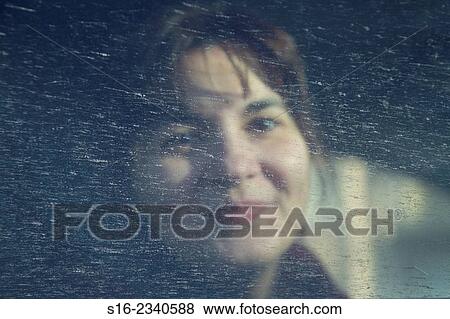 Stock Photo - Young pretty woman smiling behind a spotted splashed car window. Fotosearch