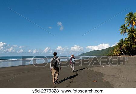 Stock Photo - "young tourists walking empty beach, wild coast of the Pacific Ocean, Corcovado National Park, Costa Rica,.". Fotosearch